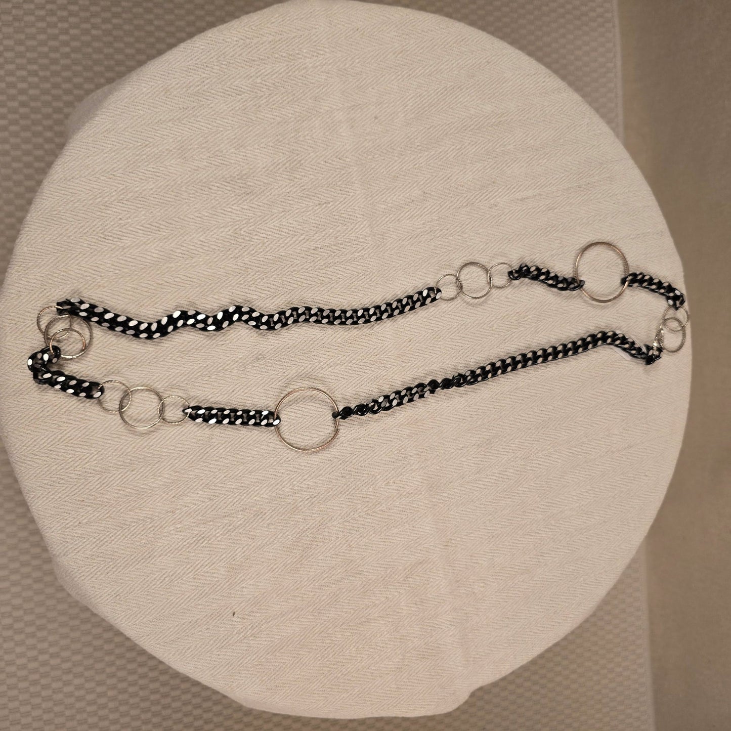 Halskette „Chain Reaction“ mit silberfarbenen Gliedern und schwarzem Stoffband mit weißen Punkten – auffälliger, flexibler Materialmix
